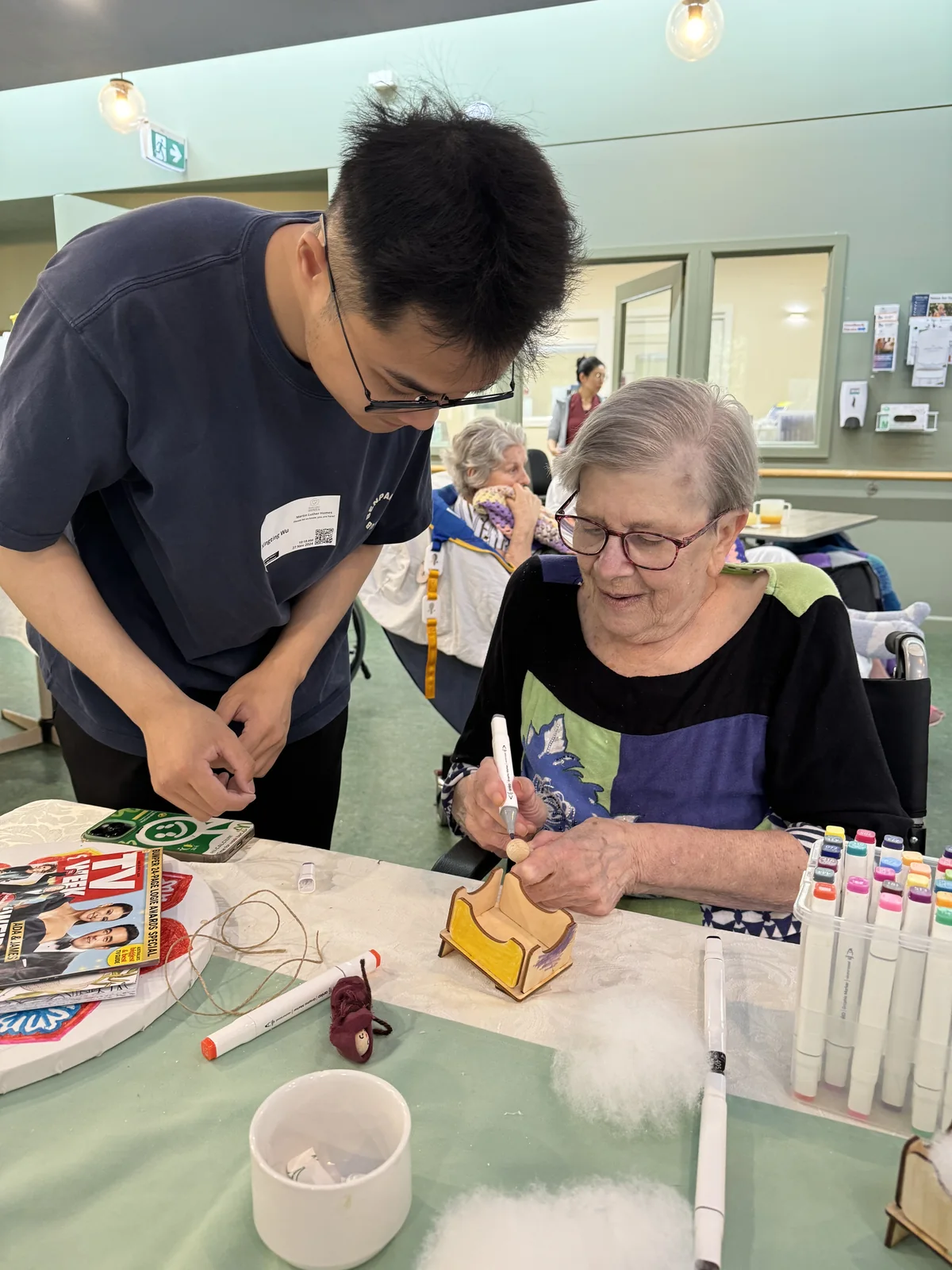 Xingting Wu working beside a resident as she decorates a wooden Nativity figure