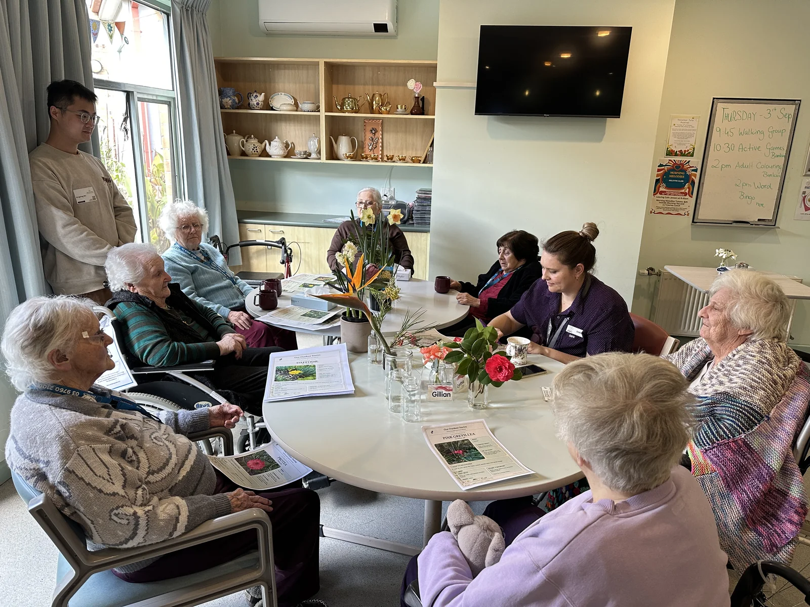 Xingting Wu with residents and care staff around tables with flowers and plant cards